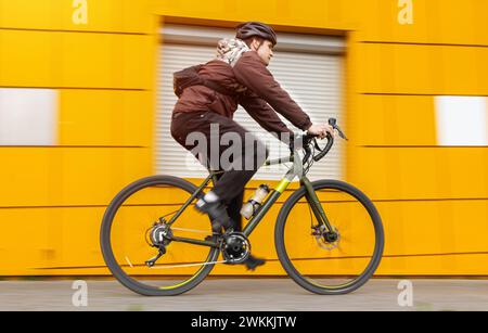 A guy on a gravel bike rides past a yellow wall. Motion blur effect. Active sport concept. Stock Photo