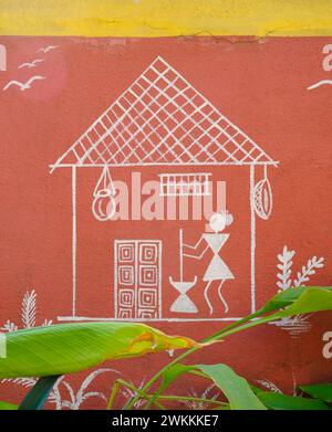 Warli tribal illustration depicting a woman pounding grain in front of a hut painted on a garden wall Stock Photo