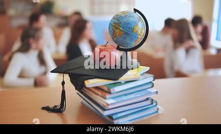 A globe of the world with textbooks and a college graduate's cap in a school classroom during class. Stock Photo