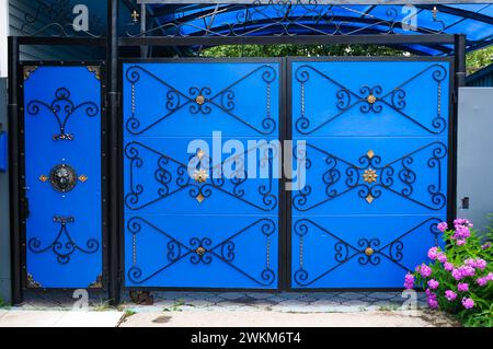 August 7, 2021 Europe, Russia, Tver region. Blue metal gates with beautiful ornaments. Blue metal gates with gold forged pattern of symmetrical parts. Stock Photo