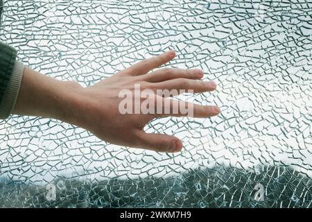 Hand touching broken glass window. Close-up view of shattered glass with cracks and texture. Safety and security concept with copy space for design and print Stock Photo