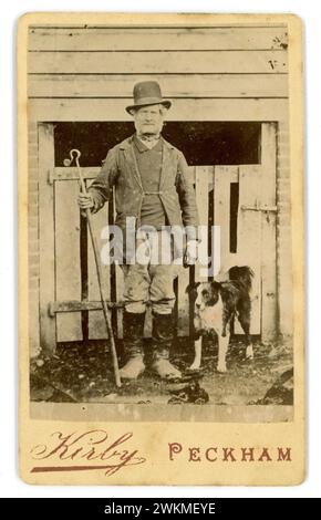 Original Victorian Carte de Visite (visiting card or CDV) of working class man - a drover / shepherd wearing tall crowned bowler hat, carrying a crook, wearing leather boots with buttoned gaiters, with his faithful collie sheepdog. The man may have driven his sheep bound for the meat markets of London such as Smithfields, from as far away as Wales following ancient drovers routes. Possibly a Welshman. Many drovers grazed their animals on the Common at Peckham village before going on to London. Photographer - Theophilus Claudius Kirby (1829-1907) Peckham, S.E. London, Borough of Southwark, U.K. Stock Photo
