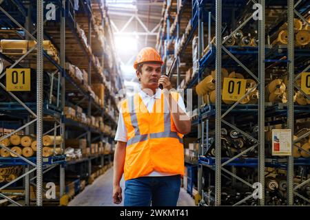 Warehouse worker in protective helmet talking on walkie talkie. Stock Photo