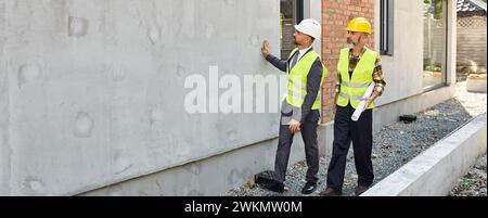 good looking cottage builder and architect with blueprint discussing construction process, banner Stock Photo