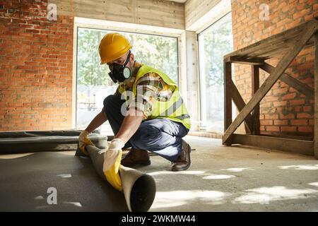 hardworking construction worker in safety helmet and gloves with dust mask putting carpet on floor Stock Photo