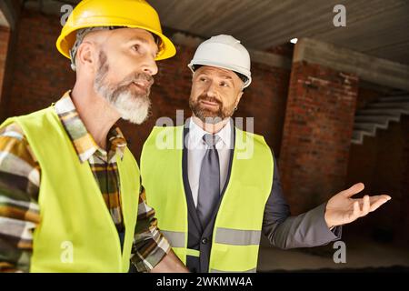 good looking jolly cottage builder and architect discussing their work on construction site Stock Photo