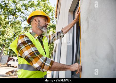 good looking hardworking construction worker with beard measuring window with tape, cottage builder Stock Photo