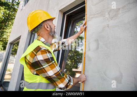 good looking hardworking construction worker with beard measuring window with tape, cottage builder Stock Photo