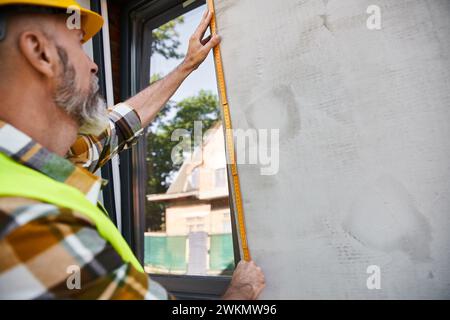good looking hardworking construction worker with beard measuring window with tape, cottage builder Stock Photo