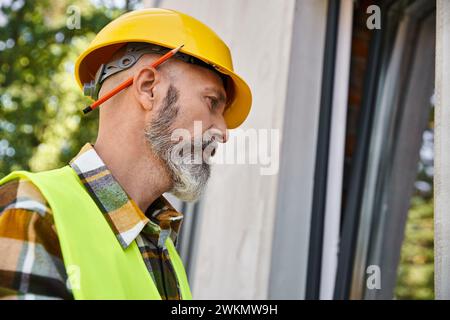 good looking dedicated cottage builder in safety helmet looking at window while on construction site Stock Photo