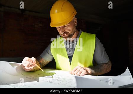good looking builder in safety vest and helmet working on his blueprint before construction Stock Photo
