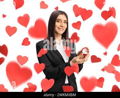 Young woman standing under falling hearts and holding a box with a ring isolated on white background Stock Photo