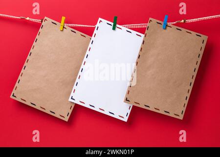 Three congratulatory envelopes attached with clothespins and hanging on a rope on a red background, template for designer Stock Photo