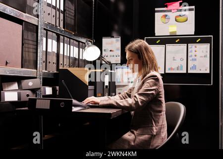 Woman manager typing administration report on laptop computer, working overtime at management research in file room. Bookkeeper checking accountancy record, searching for business documentation Stock Photo