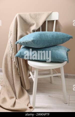 Soft pillows and warm blanket on chair indoors Stock Photo