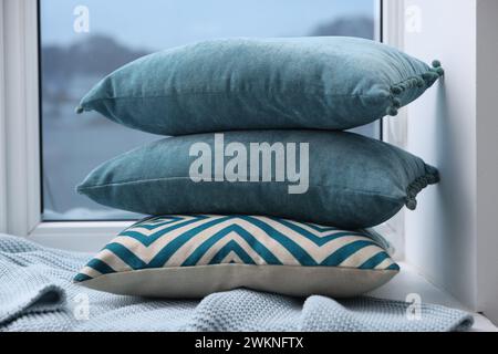 Stack of soft pillows and blanket on window sill indoors Stock Photo