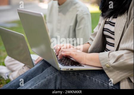 A close-up shot of two college students collaborating on work and using their laptop computer in a campus park. university students, uni life, school Stock Photo