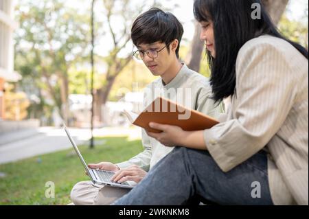 Two young Asian university students are sharing their ideas, preparing for an exam, or collaborating on a project together in the university park. Stock Photo