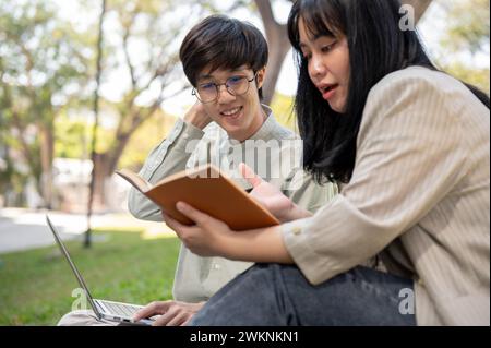 Two young Asian university students are sharing their ideas, preparing for an exam, or collaborating on a project together in the university park. Stock Photo
