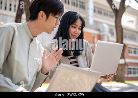 Two smart Asian university students are discussing and collaborating on a project while sitting together on a bench in the university park. university Stock Photo