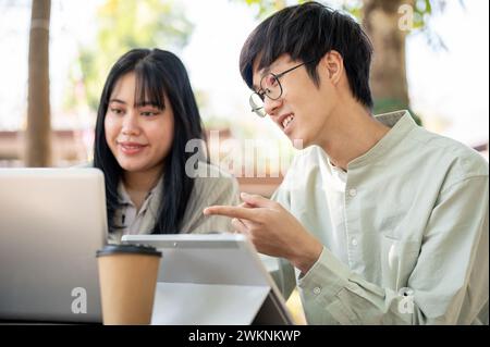 Two Asian male and female colleagues are discussing and collaborating on work together at a cafe. working remotely and teamwork concepts Stock Photo