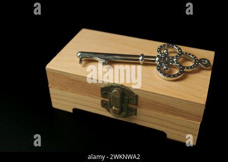 Closed wooden box with a metal key on top isolated on black background and copyspace Stock Photo
