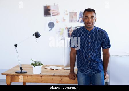 Man, portrait and desk at creative studio or startup as .graphic designer with photographs, project planning or magazine. Male person, face and Stock Photo