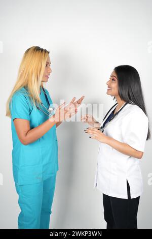 Two female medical professionals conversing, wearing scrubs and white tops, against a neutral gray backdrop Stock Photo