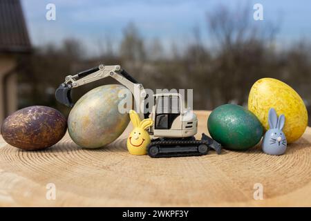model of a toy gray excavator and multi-colored Easter eggs on a wooden stump Stock Photo