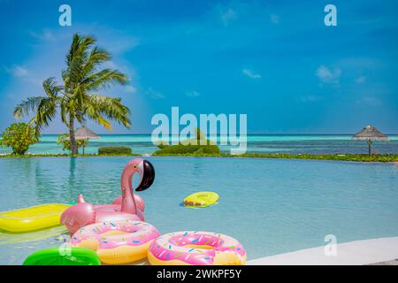 Inflatable rings and mattress floating in infinity swimming pool. Summer view vacation, tropical resort outdoor landscape, fun happy island beach Stock Photo