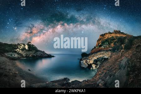 Amazing starry night sky with the majestic Milky Way over a scenic coast at a bay. A majestic landscape with cliffs and illuminated ruins Stock Photo