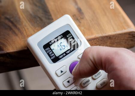 Finger of a man using the control of an air conditioner that reads sixteen degrees. Stock Photo