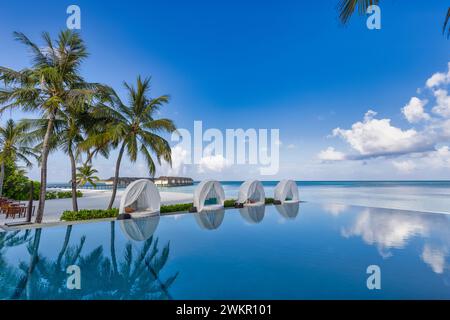 Luxury infinity pool spa with loungers tranquil palm trees exotic resort. Leisure happy summer beach landscape sunny romantic chairs umbrella sea view Stock Photo
