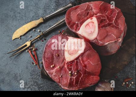 raw Ossobuco. Veal shanks Ossobuco with pepper, lemon and garlic for gremolata, typical ingredients of Italian Lombard cuisine, top view on dark backg Stock Photo