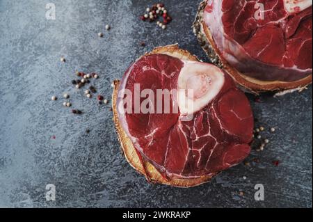 raw Ossobuco. Veal shanks Ossobuco with pepper, lemon and garlic for gremolata, typical ingredients of Italian Lombard cuisine, top view on dark backg Stock Photo