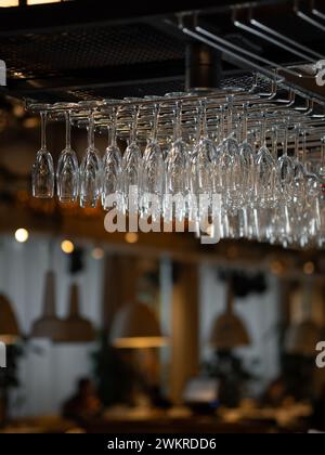 Row of clean glass in bar. Moody aesthetic image of bar and restaurant atmosphere with warm lightening and mane empty wine glasses. Row of clean polished wineglasses hanging in modern bar Stock Photo