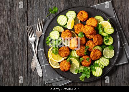 fried rice cutlets, rice tikki, indian style on black plate served with cucumber, lemon, lime slices and forks on dark wooden table, flat lay, free sp Stock Photo