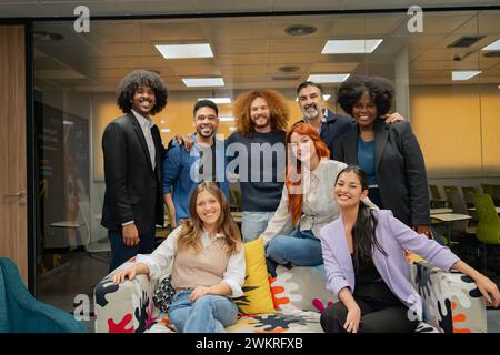 Diverse group of professionals smiling and posing together in a modern office lounge, showing team spirit and collaboration.  Stock Photo