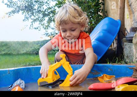 A little boy is playing with a digger on a sandpit with water Stock Photo