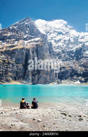 Family sitting at the edge of Oeschinen Lake (Oeschinensee) and with Blüemlisalp mountain in background, Switzerland Stock Photo