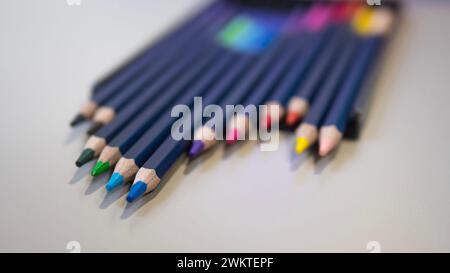 A variety of colored pencils are neatly arranged in a row on a table, resembling a colorful array of office supplies Stock Photo