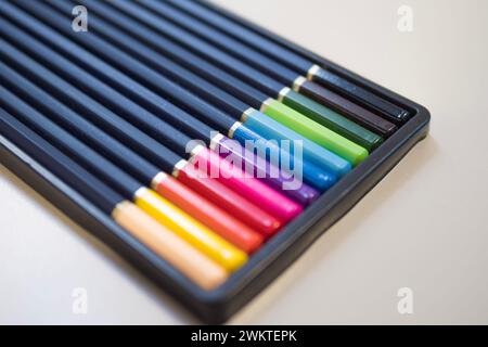 A variety of colored pencils are neatly arranged in a row on a table, resembling a colorful array of office supplies Stock Photo