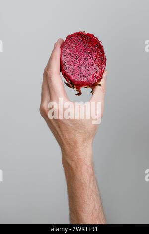 Half of Ripe Dragon fruit, Pitaya or Pitahaya in human hand on gray background, healthy food concept Stock Photo