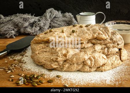 Raw sourdough dough on a wooden board with pumpkin seeds and kitchen utensils Stock Photo