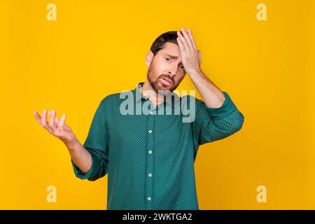 Photo of upset forgetful man with stylish haircut dressed dotted shirt holding palm on forehead isolated on yellow color background Stock Photo
