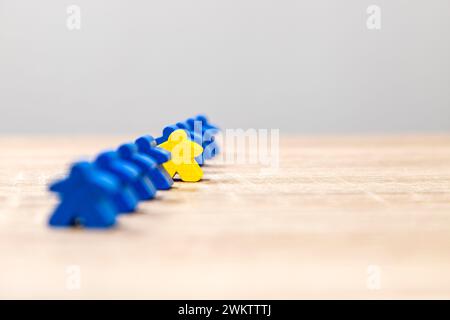 A yellow game piece positioned ahead of a row of blue pieces on a wooden background, symbolizing leadership. Stock Photo