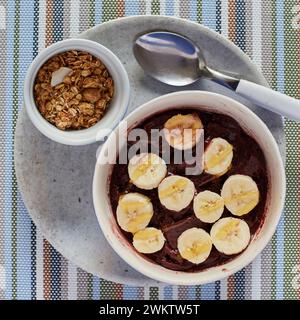 A Brazilian acai served with slices of banana and honey, in a pot on the side we can see granola and pieces of coconut Stock Photo