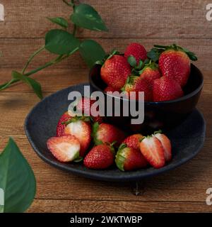 Fresh whole and cut strawberries, inside a dark plate Stock Photo