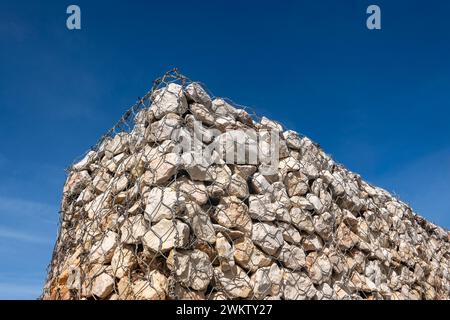 Gabion wall stone in metal wire box cage against a blue sky Stock Photo