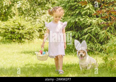 Family Easter egg hunt. Girl and dog gather colorful eggs in bascket Stock Photo